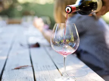 Red wine is poured into a wine glass on a table.