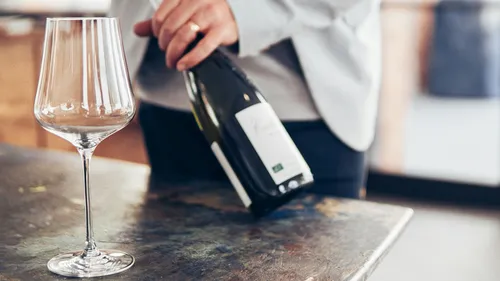 Person holds wine bottle near empty glass.