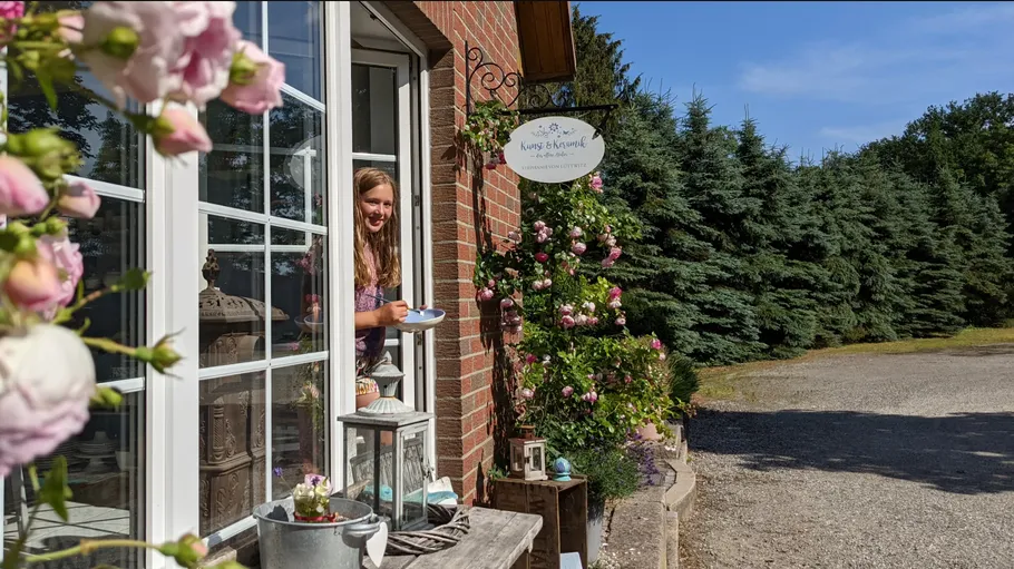 Frau hält Tasse am blumengeschmückten Fenster.
