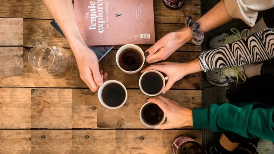 Hände halten Kaffeetassen über Holztisch.