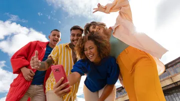 Group taking selfie outdoors, smiling happily.