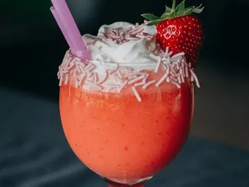 Icy strawberry drink with cream and sprinkles in a glass.