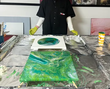 Artist with green acrylic paintings on table.