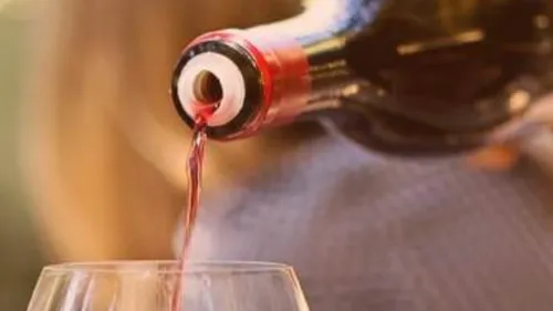 Weinflasche schenkt Rotwein in Glas ein.
