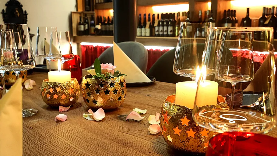 Kerzengedeckter Tisch mit Weingläsern und Blütenblättern.