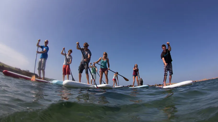 Group paddleboarding on calm ocean water.