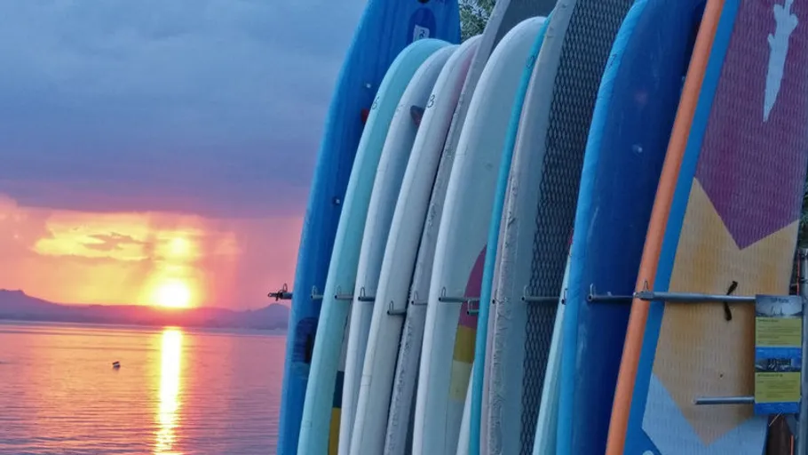 Surfbretter gestapelt neben Sonnenuntergang über Wasser.