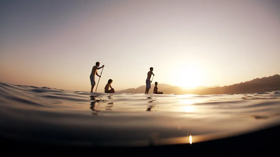 People paddleboarding on calm water at sunset.