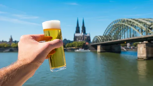 Hand holding beer by Cologne Cathedral and bridge.