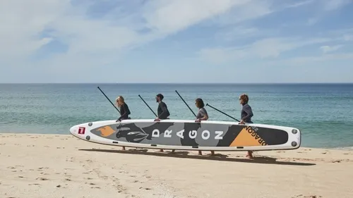 Four people carrying paddleboard on the beach.