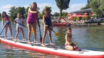 Group paddleboarding on a lake near a cafe.