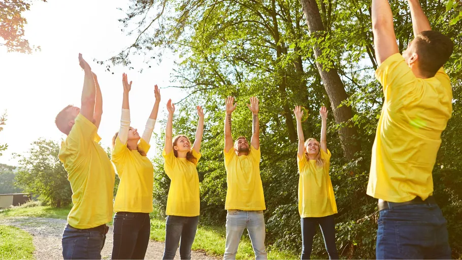 Group stretching arms upward in outdoor setting.