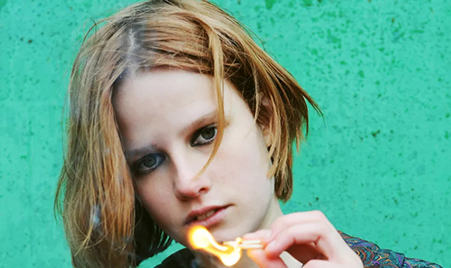 Person holds lit match against green background.