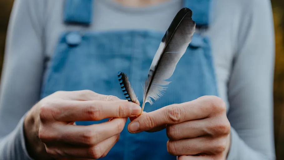 Person holding two feathers outdoors.