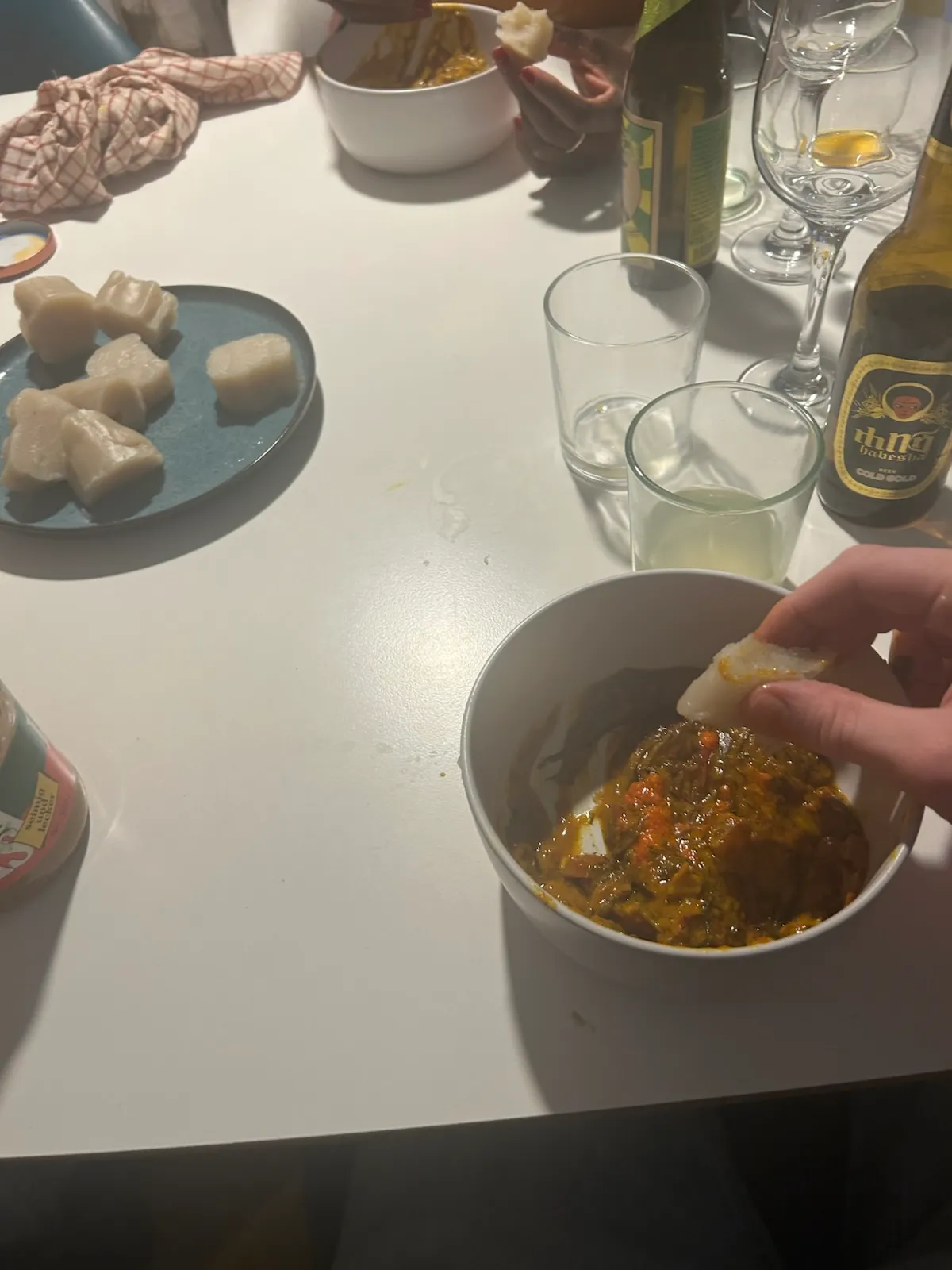 Hands eating stew with dumplings on table.