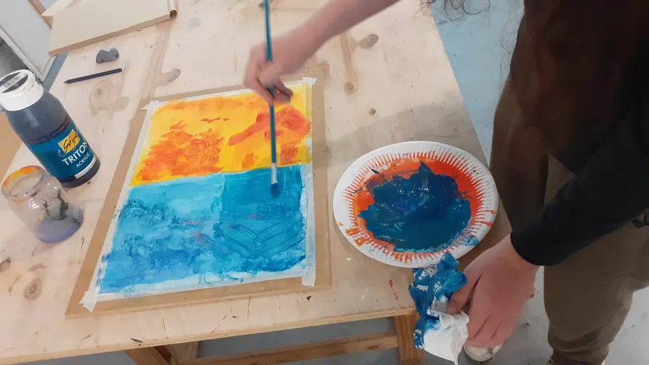 Person malt buntes Kunstwerk auf Tisch.