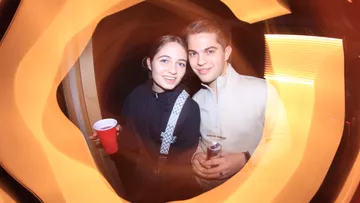 Two people smiling, holding drinks at party.