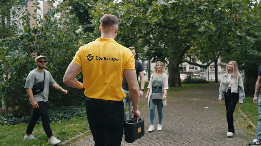Person führt Gruppe im Park, hält Koffer.