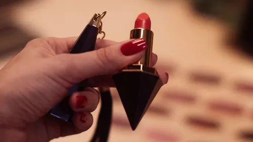 Hand hält einen Lippenstift mit roten Nägeln.