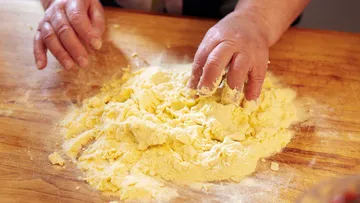 Hands kneading dough on wooden surface.