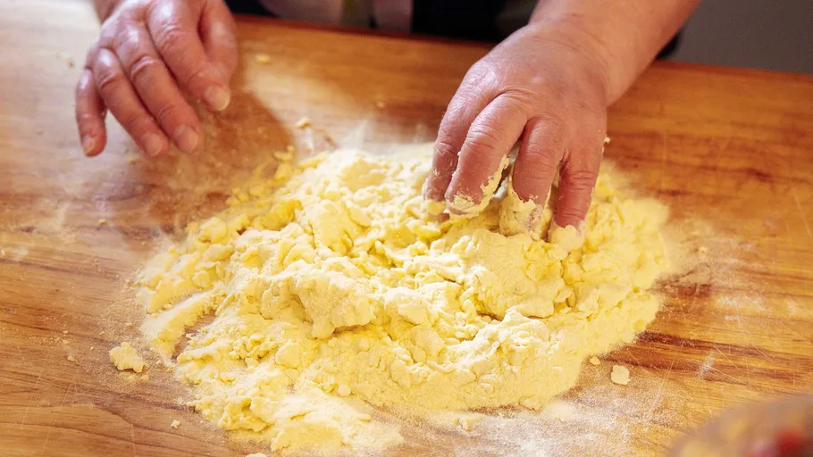 Hands kneading dough on wooden surface.