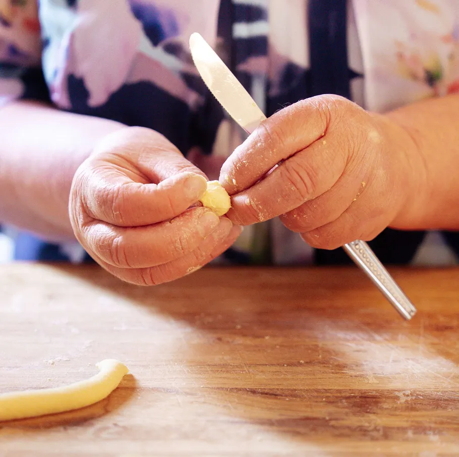 Hands shaping dough on a wooden surface.