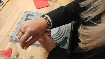 Person adjusting bracelets at wooden table.