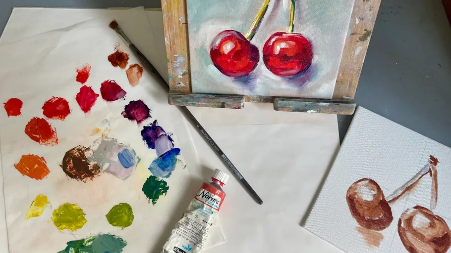 Painting of cherries with brushes and paint nearby.