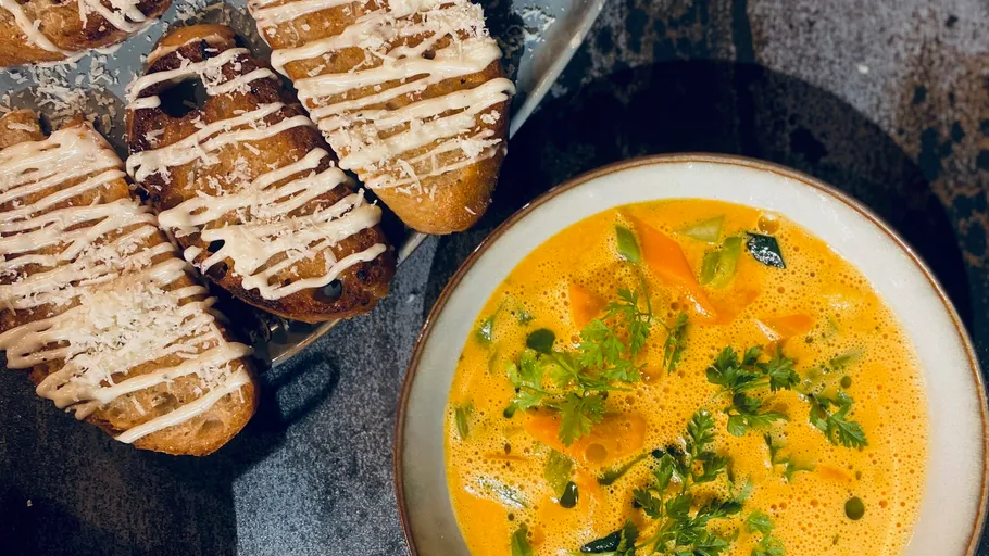 Suppe mit Gemüse neben Brotscheiben.