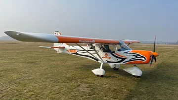 Small orange aircraft parked on grassy airfield.