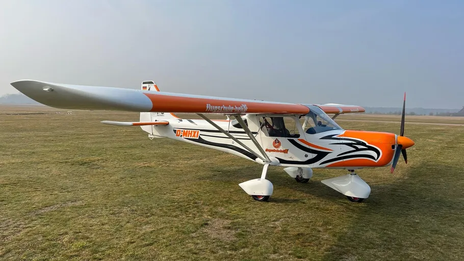Kleines oranges Flugzeug auf Graspiste geparkt.