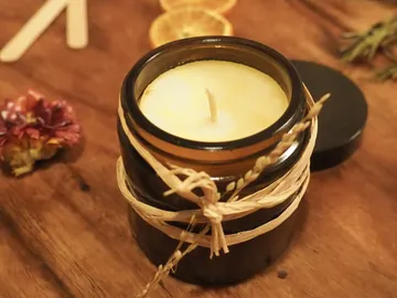 Glasbehälter mit Kerze, umgeben von Trockenblumen und Holz.