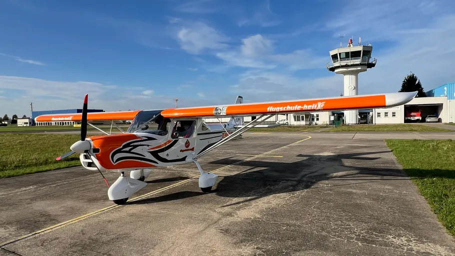 Kleines weiß-oranges Flugzeug auf Flugplatz.