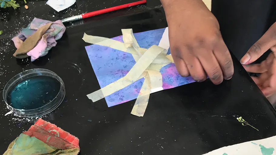Hand arranging tape on paper with art supplies.