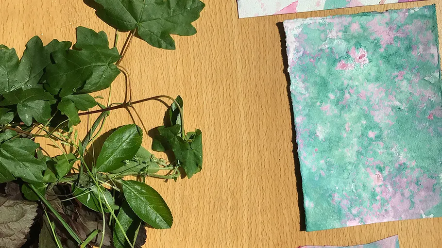 Grüne Blätter auf Holztisch mit buntem Papier.