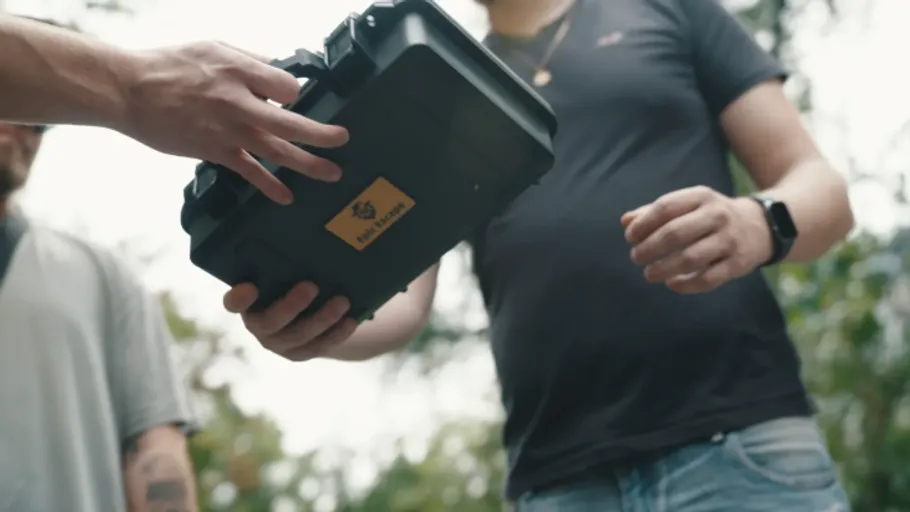 Person hands a black case outdoors.