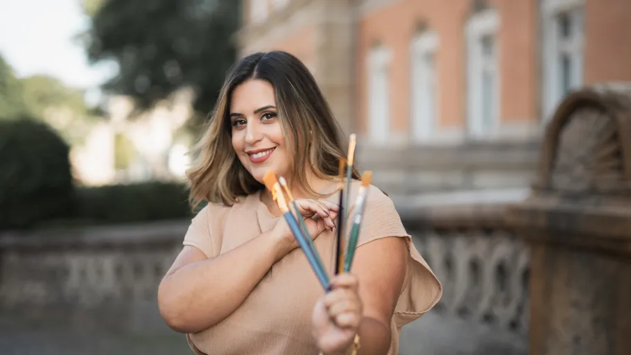 Person smiling holding paintbrushes outdoors.