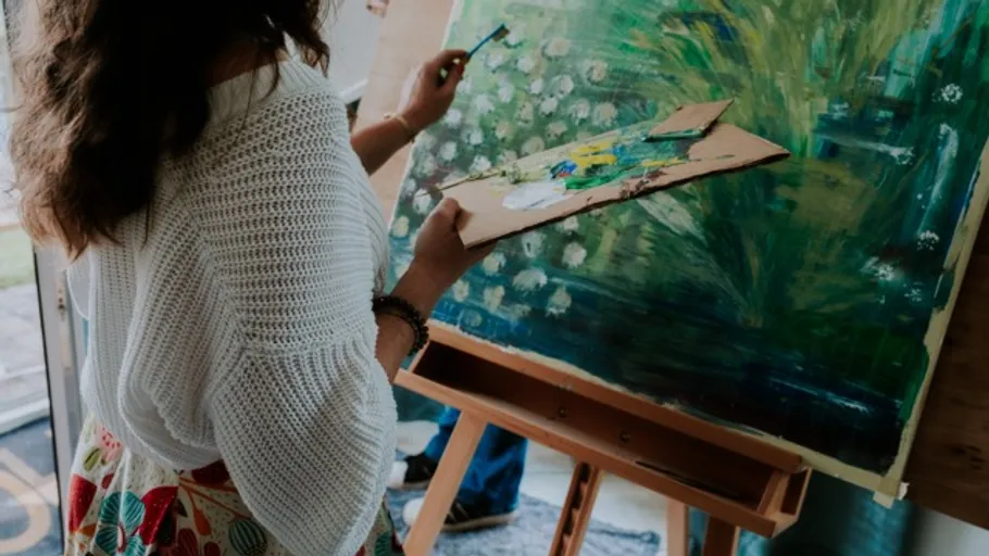 Person painting on canvas with palette indoors.