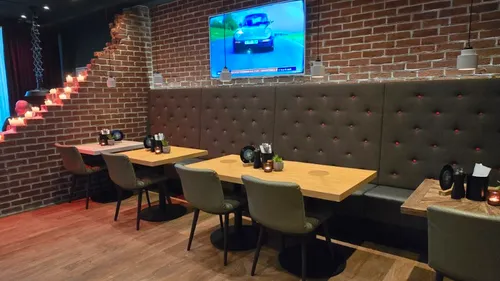 Restaurant-Sitzbereich mit Tischen, TV an Ziegelwand.