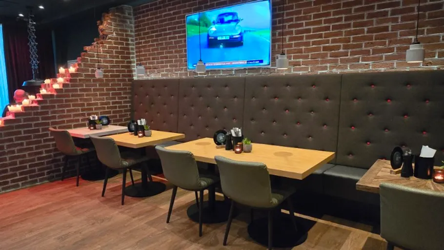 Restaurant-Sitzbereich mit Tischen, TV an Ziegelwand.