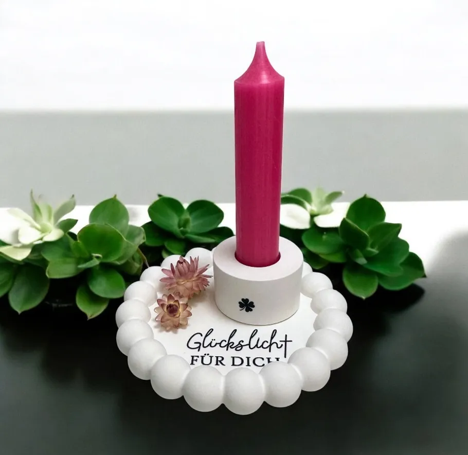 Pink candle in holder with plants around.