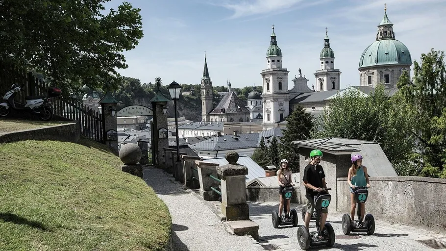 Drei Personen auf Segways blicken auf historische Gebäude.