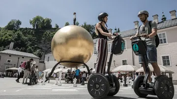 Zwei Personen fahren Segways nahe goldener Skulptur.