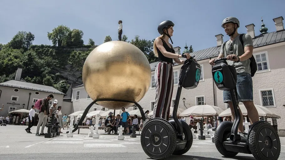Zwei Personen fahren Segways nahe goldener Skulptur.