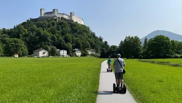 Two people ride Segways toward a hilltop castle.