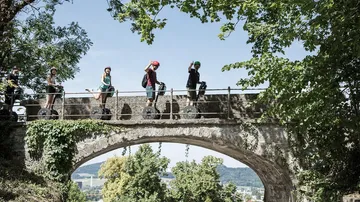 People riding Segways on a leafy bridge.