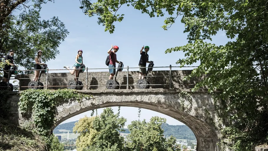 Personen fahren Segways auf einer grünen Brücke.