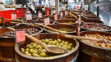 Various olives in wooden barrels at a market.