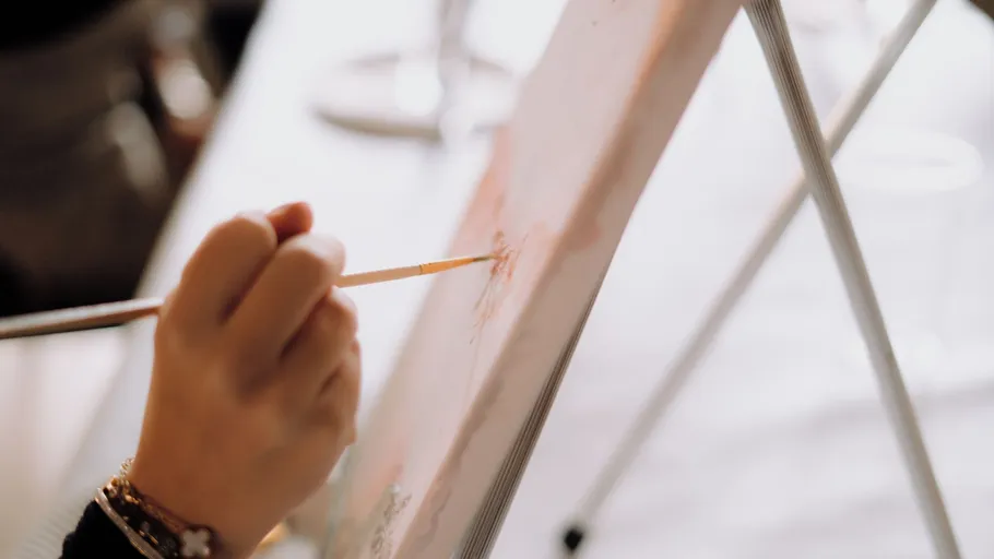 Hand painting on canvas with paintbrush indoors.