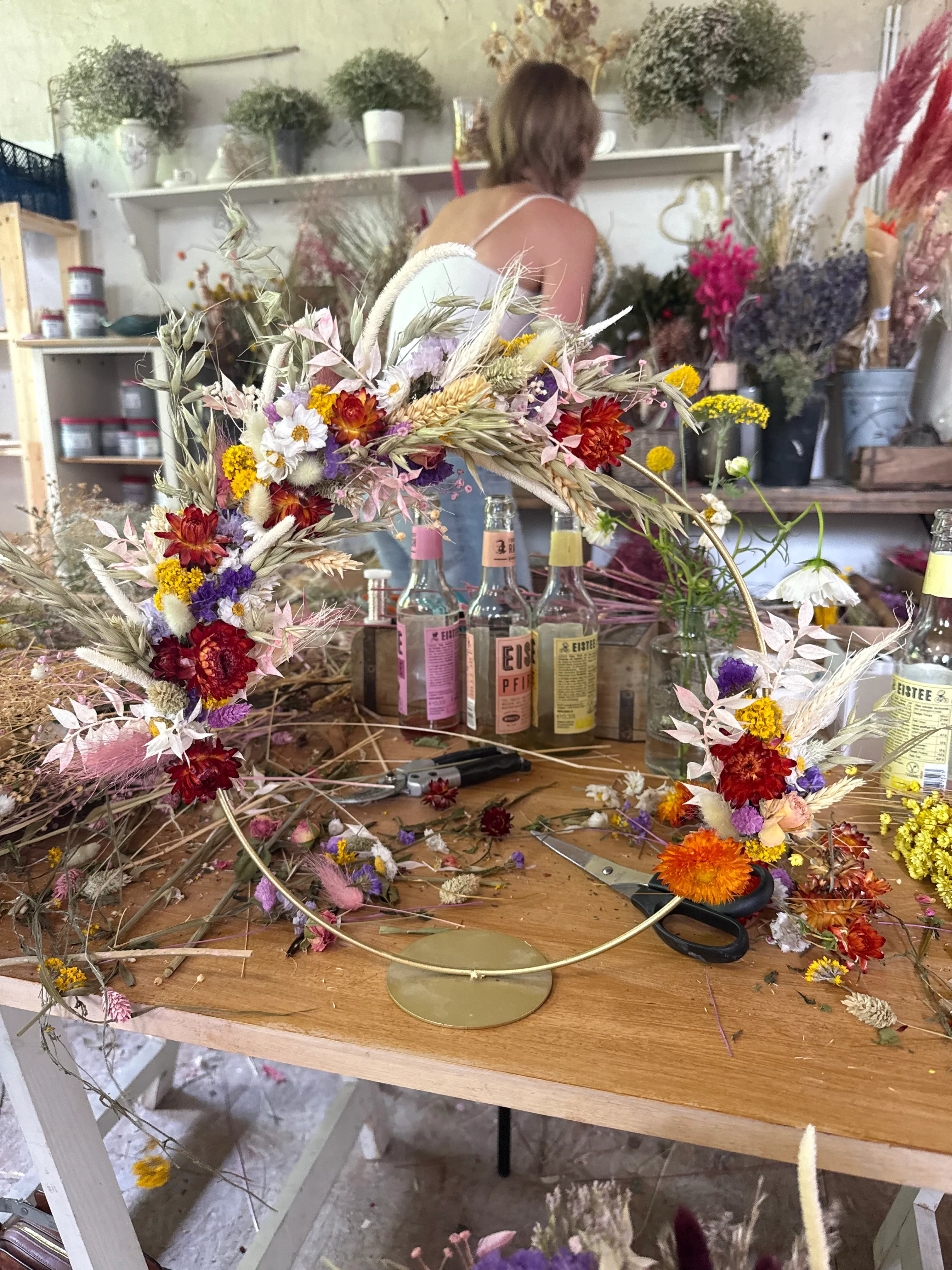 Floral wreath on table, person arranging flowers.
